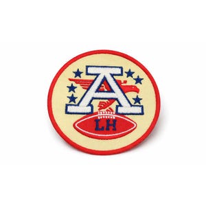 May include: A circular patch with a cream-colored background and a red border. The patch features a large white letter "A" with blue stars and a red eagle. A red football with "LH" is at the bottom.