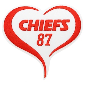 May include: A heart-shaped embroidered patch with a white background and a thick red border. The text CHIEFS is embroidered in red capital letters across the center, with the number 87 embroidered in red directly below the text.