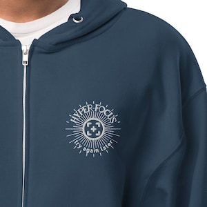 Può includere: Una felpa con cappuccio blu scuro con cerniera e un logo ricamato bianco che dice "HYPER FOCUS" con un design a raggiera e le parole "try again later" sotto.