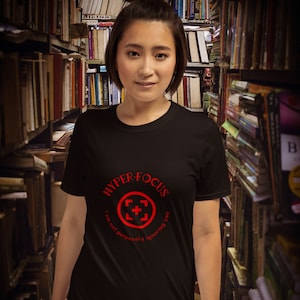 Op de afbeelding: Een zwart T-shirt met een rode cirkelvormige afbeelding met de tekst "HYPER FOCUS I am not purposely ignoring you".