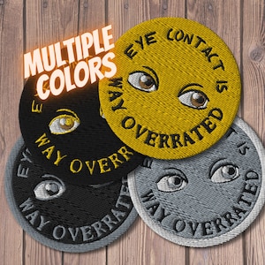 May include: Four embroidered patches with the text "Eye Contact is Way Overrated" in black lettering. The patches are in different colors: yellow, black, gray, and white.
