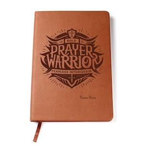May include: Brown leather journal with a laser engraved design that says "Bold Prayer Warrior Fearless Intercessor" with a cross and sword. The journal has a place for a name to be added.