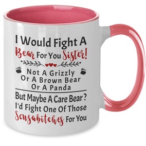May include: White ceramic mug with a pink interior and handle. The mug features the text "I Would Fight A Bear For You Sister!" in black and red, with paw prints and heart accents. A humorous gift.