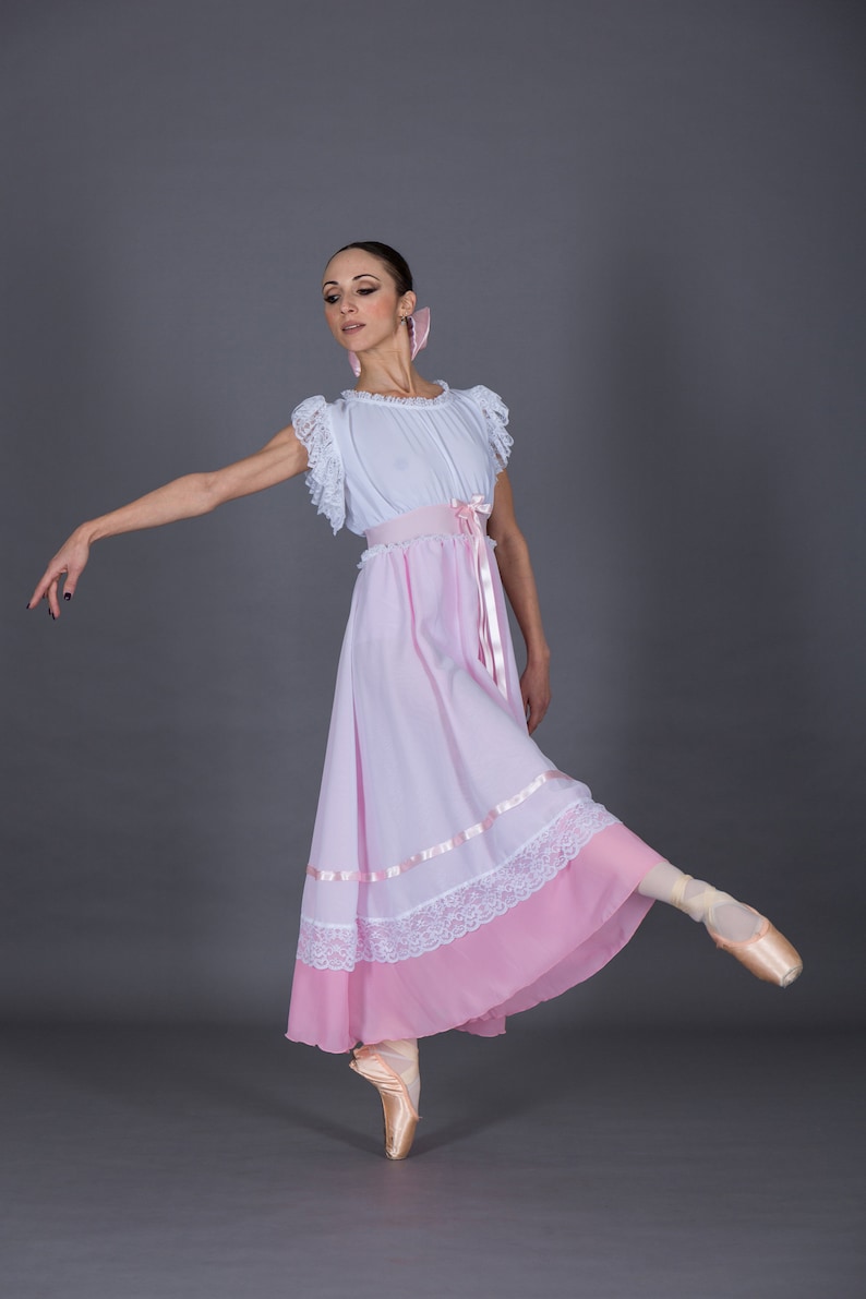 May include: A ballerina wearing a white and pink dress with lace trim and a pink ribbon around the waist. She is standing on one foot with her other leg extended to the side. She is wearing pink ballet shoes.
