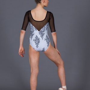 K&ouml;nnte beinhalten: Hellblaues Trikot mit schwarzem Mesh-Ausschnitt und &Auml;rmeln. Das Trikot hat ein florales Muster in Dunkelblau. Das Model tr&auml;gt Ballettschuhe. Der Hintergrund ist einfarbig grau.