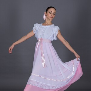 May include: A ballerina wearing a white and pink dress with a pink ribbon belt and lace trim. She is wearing pink ballet shoes and has a pink ribbon in her hair.