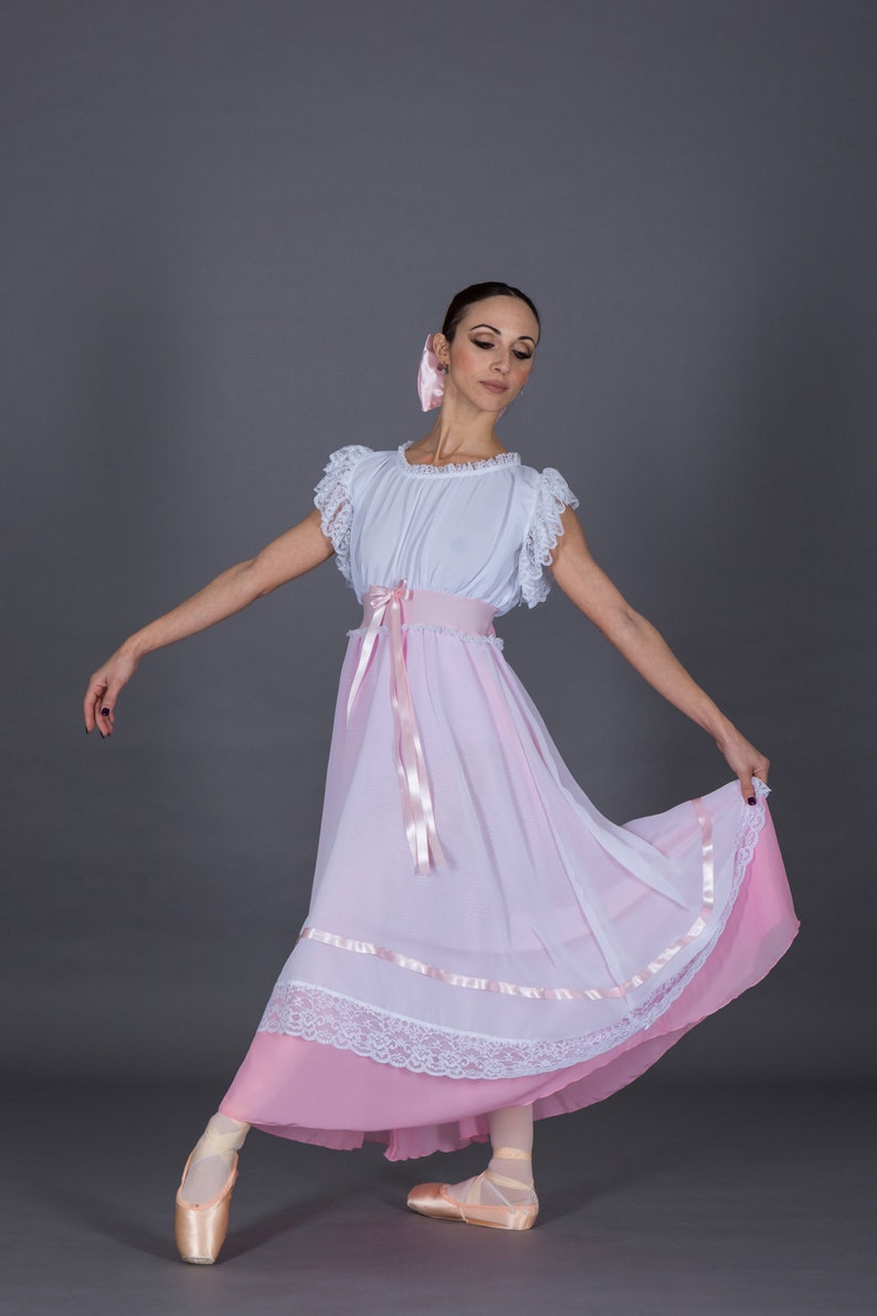 May include: A ballerina wearing a white and pink dress with a pink ribbon belt and lace trim. She is wearing pink ballet shoes and has a pink ribbon in her hair.