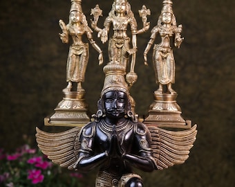 May include: A gold and black metal statue of a kneeling deity with wings. The deity has a crown and is holding hands in a prayer position. Three smaller gold statues of deities stand on a platform above the kneeling deity.
