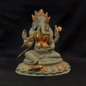 Op de afbeelding: Een groen en gouden Ganesha-beeld met een decoratieve basis. Het beeld staat op een zwarte ondergrond.