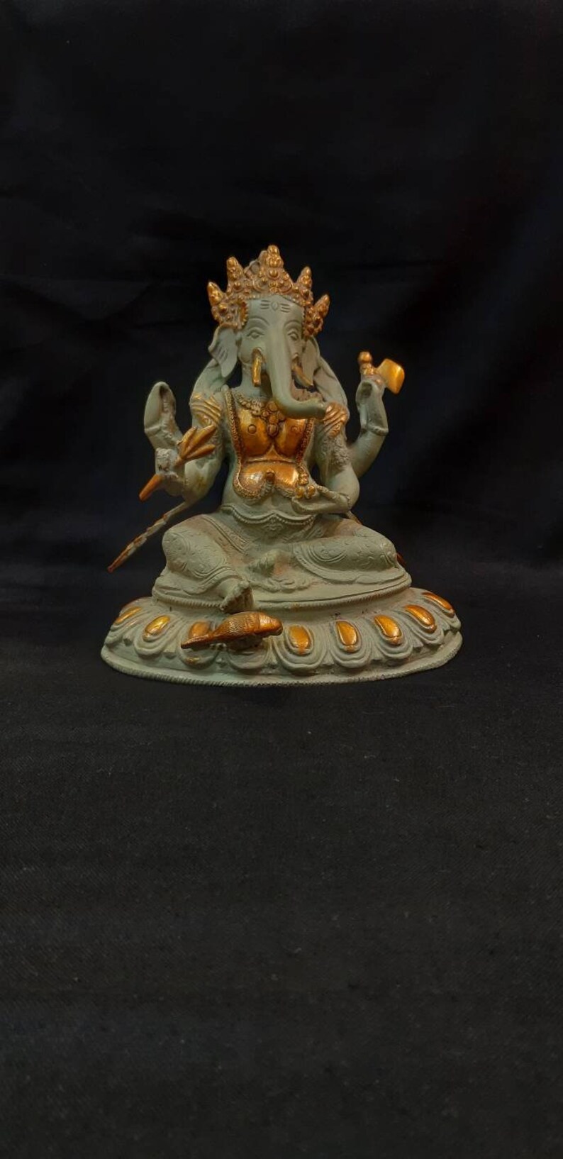 Op de afbeelding: Een groen en gouden Ganesha-beeld met een vierarmige pose, zittend op een lotusbasis met gouden accenten.
