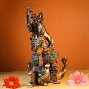 May include: A gold-colored statue of Ganesha, the Hindu god of wisdom and prosperity, sitting on an elephant. The statue is decorated with colorful gemstones and intricate details.