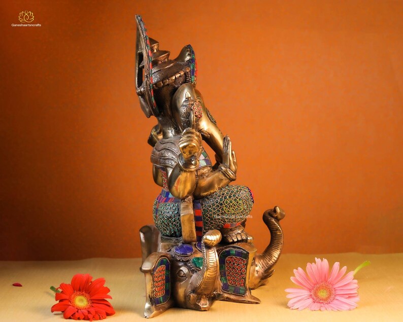 May include: A gold-colored statue of Ganesha, the Hindu god of wisdom and prosperity, sitting on an elephant. The statue is decorated with colorful gemstones and intricate details.