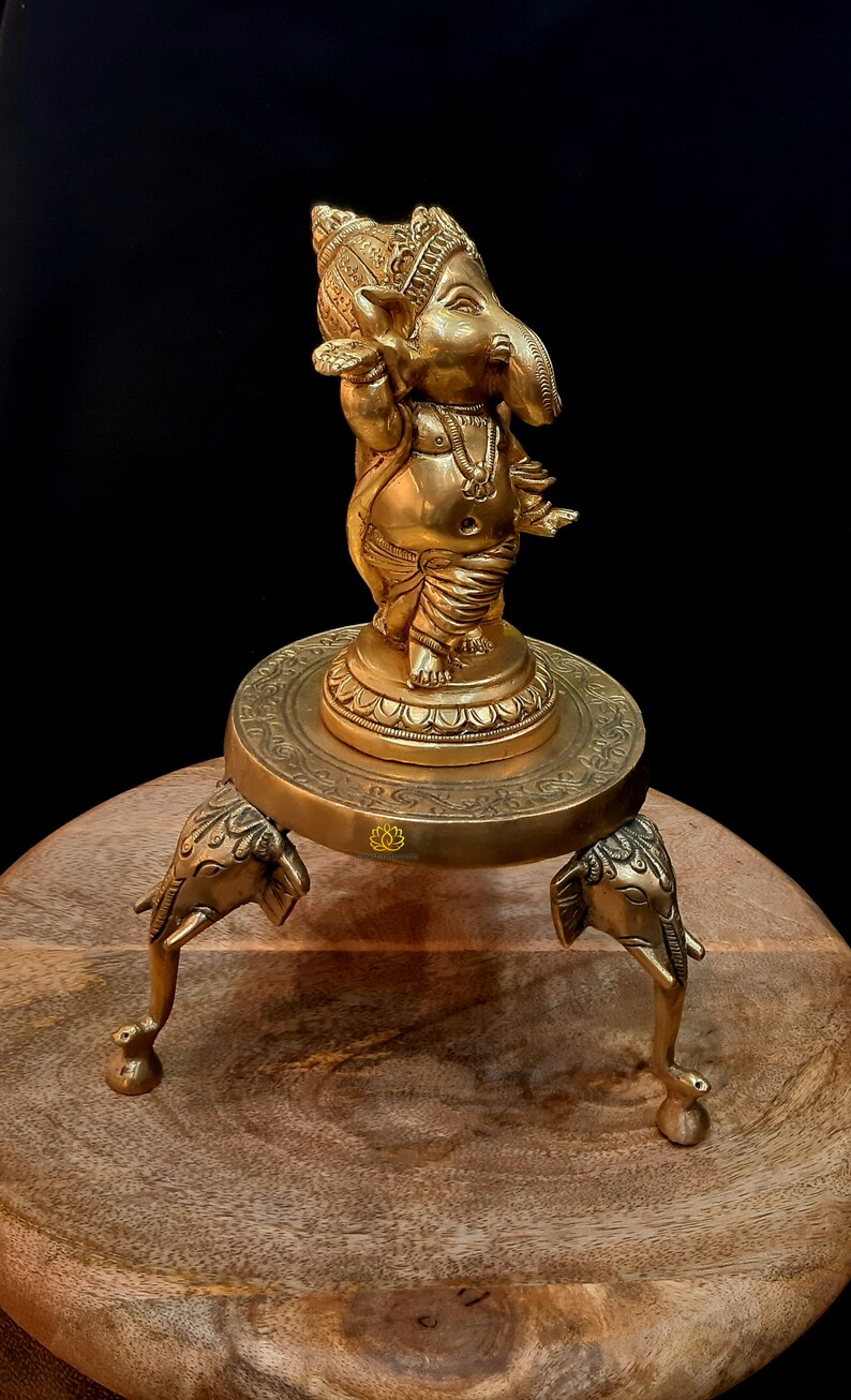 Puede incluir: Una estatua de bronce dorado de Ganesha, el dios hind&uacute; de la sabidur&iacute;a y la prosperidad, de pie sobre una base decorativa con tres patas de elefante. La estatua est&aacute; intrincadamente detallada y presenta un dise&ntilde;o tradicional.
