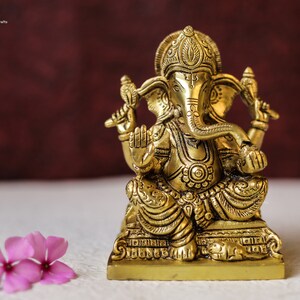 Puede incluir: Una estatua de metal dorada de Ganesha, el dios hind&uacute; de la sabidur&iacute;a y la prosperidad, sentado en un trono con una rata a sus pies.