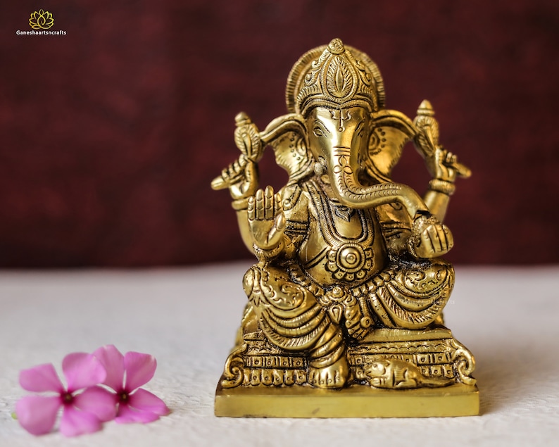 Puede incluir: Una estatua de metal dorada de Ganesha, el dios hind&uacute; de la sabidur&iacute;a y la prosperidad, sentado en un trono con una rata a sus pies.