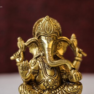 Puede incluir: Una estatua de metal dorada de la deidad hind&uacute; Ganesha. La estatua est&aacute; intrincadamente detallada con patrones florales y geom&eacute;tricos. Ganesha est&aacute; representado con cabeza de elefante, un solo colmillo y cuatro brazos.
