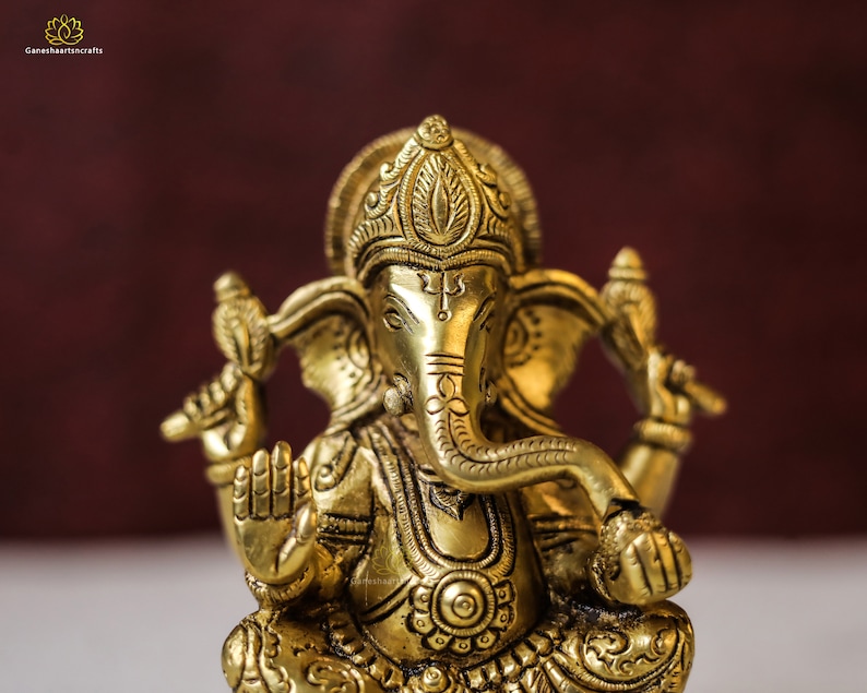 Puede incluir: Una estatua de metal dorada de la deidad hind&uacute; Ganesha. La estatua est&aacute; intrincadamente detallada con patrones florales y geom&eacute;tricos. Ganesha est&aacute; representado con cabeza de elefante, un solo colmillo y cuatro brazos.