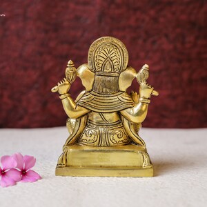 Puede incluir: Una estatua de lat&oacute;n de color dorado de la deidad hind&uacute; Ganesha, sentado en un trono. La estatua est&aacute; intrincadamente detallada con patrones florales y tiene una corona en la cabeza.