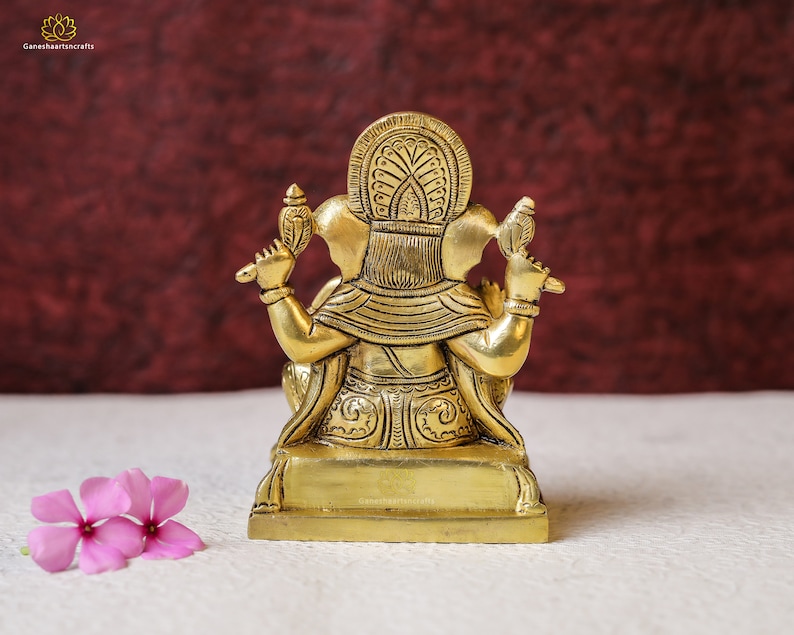 Puede incluir: Una estatua de lat&oacute;n de color dorado de la deidad hind&uacute; Ganesha, sentado en un trono. La estatua est&aacute; intrincadamente detallada con patrones florales y tiene una corona en la cabeza.