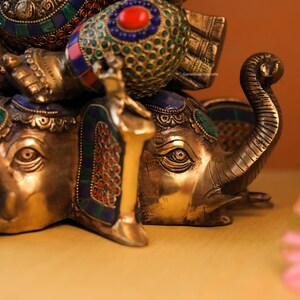 May include: A gold-colored statue of Ganesha, the Hindu god of wisdom and prosperity, riding on an elephant. The statue is decorated with colorful gemstones and intricate details.