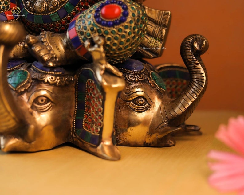 May include: A gold-colored statue of Ganesha, the Hindu god of wisdom and prosperity, riding on an elephant. The statue is decorated with colorful gemstones and intricate details.