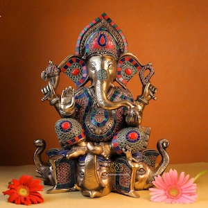 May include: A gold-colored statue of Ganesha, the Hindu god of wisdom and prosperity, sitting on a double elephant base. The statue is decorated with colorful gemstones and intricate details.