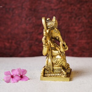 Puede incluir: Una estatua de bronce dorada de Ganesha, el dios hind&uacute; de los comienzos, sentado en un trono con una corona en la cabeza. La estatua est&aacute; intrincadamente detallada y tiene un dise&ntilde;o tradicional.
