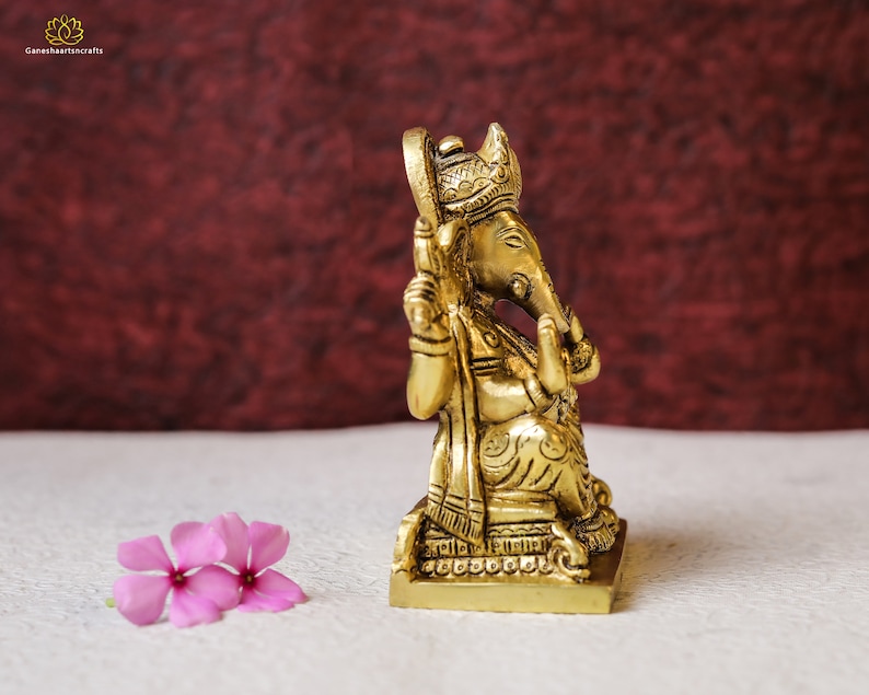 Puede incluir: Una estatua de bronce dorada de Ganesha, el dios hind&uacute; de los comienzos, sentado en un trono con una corona en la cabeza. La estatua est&aacute; intrincadamente detallada y tiene un dise&ntilde;o tradicional.