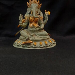 Op de afbeelding: Een groen en gouden Ganesha-beeld met een decoratieve basis. Het beeld staat op een zwarte ondergrond.