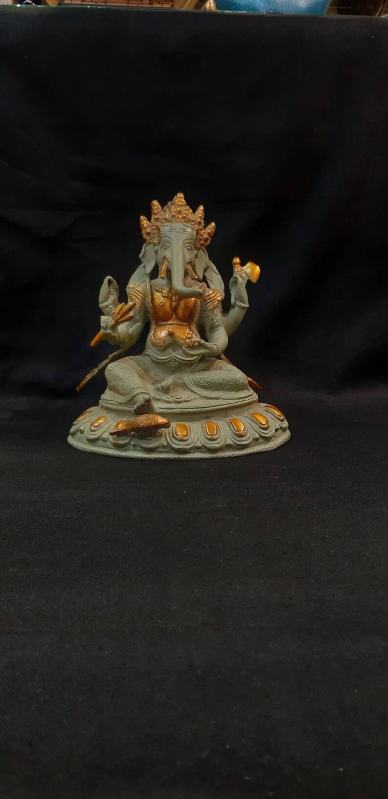 Op de afbeelding: Een groen en gouden Ganesha-beeld met een decoratieve basis. Het beeld staat op een zwarte ondergrond.