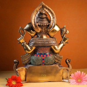 May include: A gold-colored statue of Ganesha, the Hindu god of wisdom and prosperity, with intricate details and colorful accents. The statue is sitting on a base with a lotus flower design.