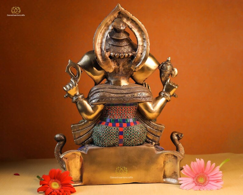 May include: A gold-colored statue of Ganesha, the Hindu god of wisdom and prosperity, with intricate details and colorful accents. The statue is sitting on a base with a lotus flower design.