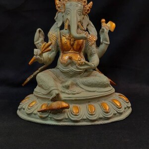 Op de afbeelding: Een groen en gouden Ganesha-beeld met een decoratieve basis. Het beeld staat op een zwarte ondergrond.