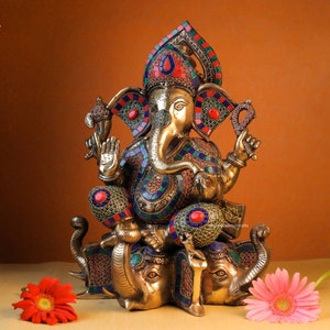 May include: A gold-toned statue of Ganesha, the Hindu god of wisdom and prosperity, sitting on three elephants. The statue is decorated with colorful mosaic tiles and gemstones.