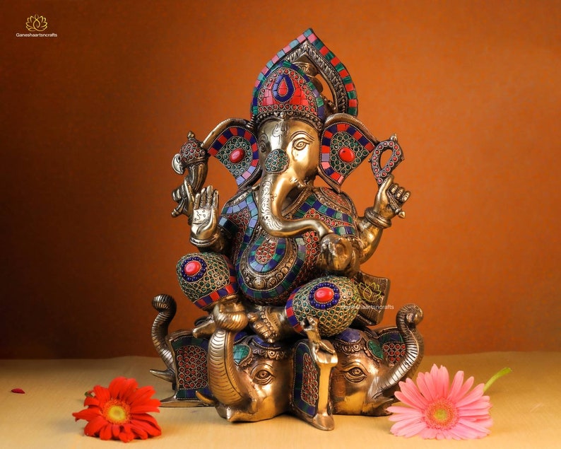 May include: A gold-toned statue of Ganesha, the Hindu god of wisdom and prosperity, sitting on three elephants. The statue is decorated with colorful mosaic tiles and gemstones.