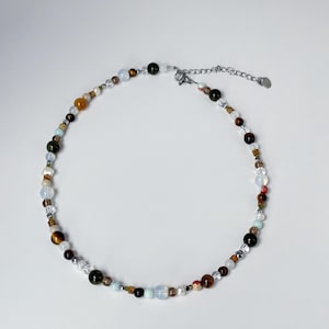 May include: A delicate necklace made of various colored beads, including brown, green, white, and blue. The necklace has a silver clasp.