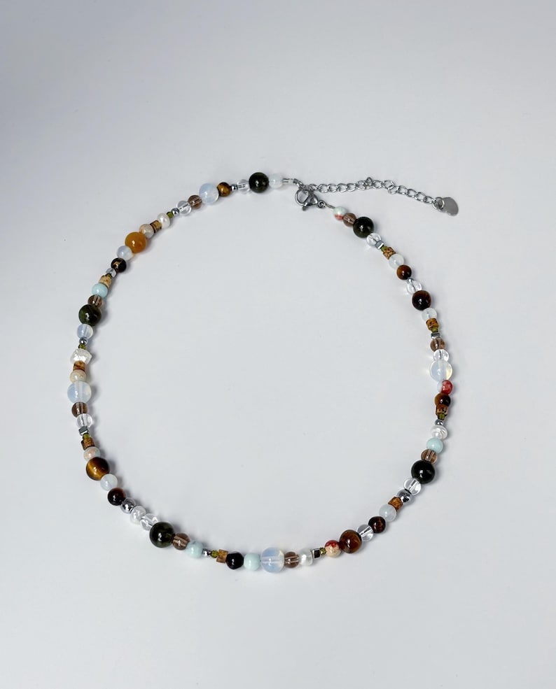 May include: A delicate necklace made of various colored beads, including brown, green, white, and blue. The necklace has a silver clasp.