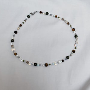May include: A multi-colored beaded necklace with green, brown, white, and gray beads. The necklace is made of natural stones and has a silver clasp.