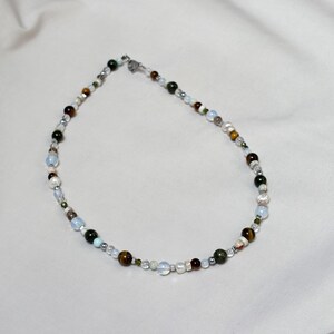 May include: A multi-colored beaded necklace with a silver clasp. The beads are various shades of brown, green, white, and gray.
