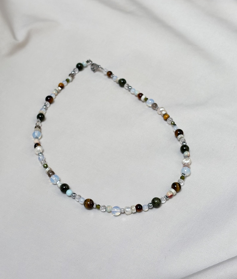May include: A multi-colored beaded necklace with a silver clasp. The beads are various shades of brown, green, white, and gray.