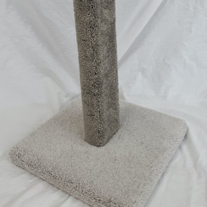 May include: A grey cat scratching post with a square base and a tall, cylindrical post covered in grey carpet.