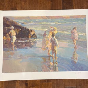 May include: A framed print of a beach scene with figures in the water. The artwork features a warm color palette with figures in the water and on the shore. The print is held in place with metal clips and a hammer.