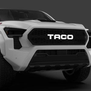 Puede incluir: Camioneta blanca de recogida con una parrilla negra y la palabra "TACO" en letras blancas en la parte delantera. La camioneta tiene ruedas negras con detalles rojos.