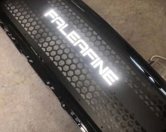 May include: Black metal grille with a honeycomb pattern and the word "FALEFINE" in white lettering.