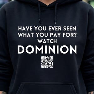 May include: Black hooded sweatshirt with the text "HAVE YOU EVER SEEN WHAT YOU PAY FOR? WATCH DOMINION" in white. A QR code is below the text. Two people in the background wear white masks and hold images.