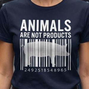Könnte beinhalten: Marineblaues T-Shirt mit dem weißen Text "ANIMALS ARE NOT PRODUCTS". Eine Schweinesilhouette ist in ein Barcode-Design integriert. Das Shirt hat auch eine Zahlenfolge am unteren Rand.