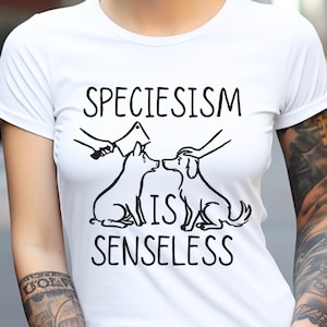 May include: White t-shirt with a black graphic that says "Speciesism is Senseless". The graphic features a pig and a dog, with the pig being held by a hand holding a butcher knife.
