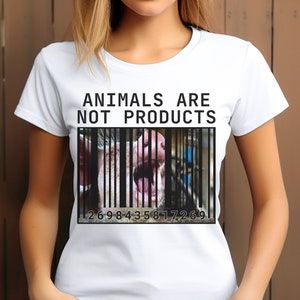 Può includere: Maglietta bianca con il testo "Gli animali non sono prodotti" e un codice a barre con il muso di un maiale dietro le sbarre. I numeri del codice a barre sono 2698435817269.