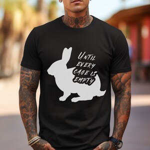 Pode incluir: Camiseta preta com uma silhueta branca de um coelho e o texto "UNTIL EVERY CAGE IS EMPTY".