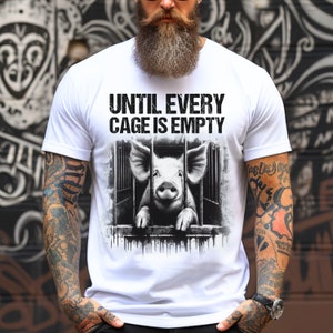 May include: White t-shirt with a black and white image of a pig in a cage. The text "UNTIL EVERY CAGE IS EMPTY" is printed on the shirt.